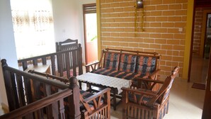 A dining area with a wooden bench and chairs, a table with a lace tablecloth, and a brick wall. - Shyni Tourist Guesthouse (Hikkaduwa)