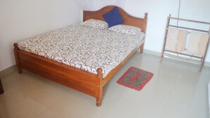 A single bed with a patterned bedspread and a blue pillow, a wooden headboard, and a red and gray rug on a tiled floor. - Shyni Tourist Guesthouse (Hikkaduwa)