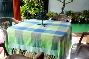 Una mesa con mantel a cuadros, rodeada de sillas, en una habitación con plantas en macetas y una pared verde.