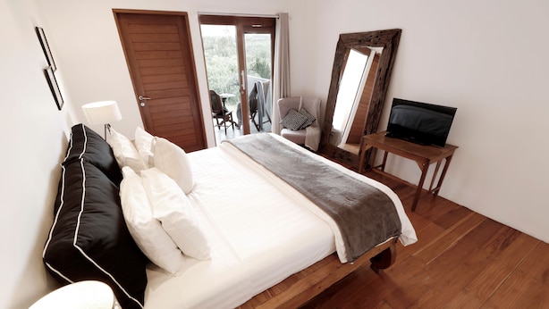 Quarto com cama de madeira, televisão sobre uma mesa de madeira e porta de vidro deslizante que dá para uma área externa.