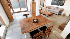 Uma área de refeições com mesa e cadeiras de madeira, um sofá e uma janela grande.