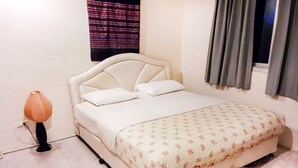 Ein ordentlich bezogenes Bett mit Blumenoptik, eine Nachttischlampe und ein Fenster mit Vorhängen.