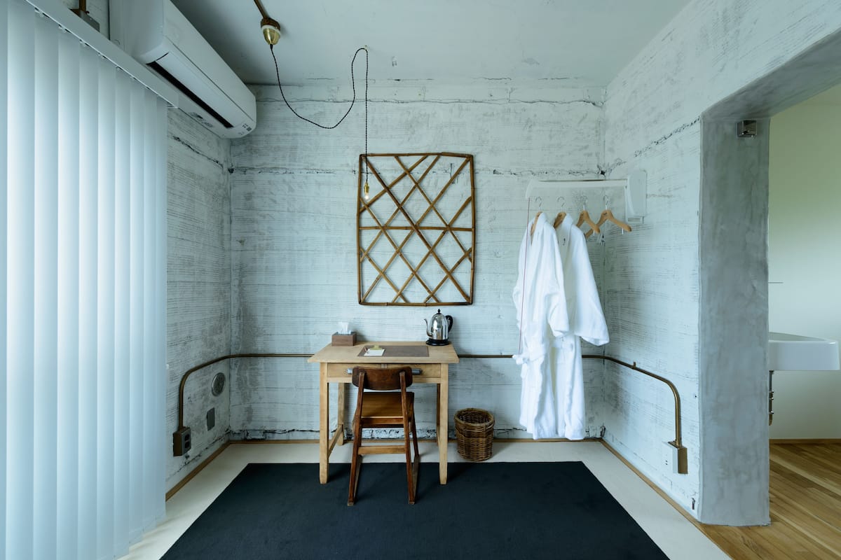 A small, rustic bathroom with a wooden desk, a chair, a hanging light fixture, and a towel rack with towels.