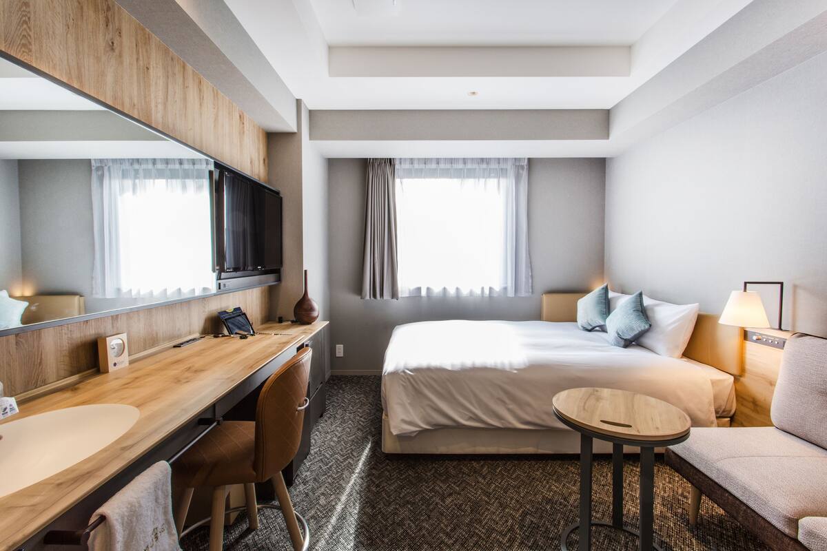 Une chambre d’hôtel avec un bureau en bois, un lit avec des oreillers, un canapé, une table ronde et un grand miroir.