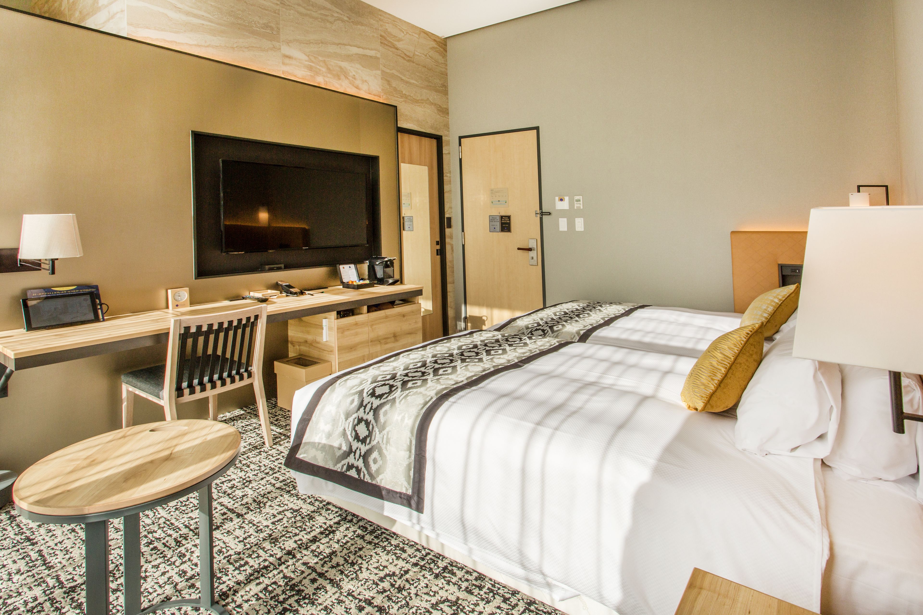 Habitación de hotel con cama, escritorio con computadora, silla, televisor y cafetera.