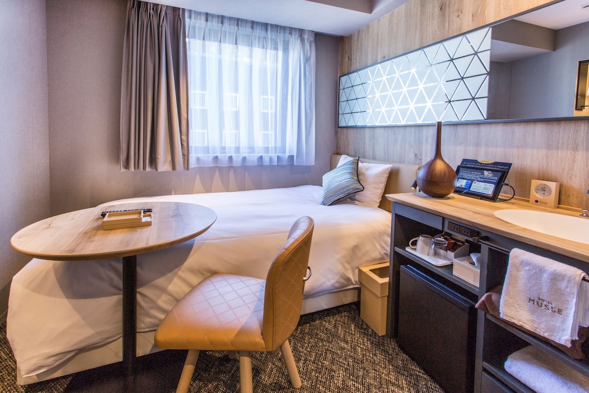 Une chambre d’hôtel comprenant un lit, une table ronde, une chaise, un bureau avec un ordinateur, un lavabo et un miroir.
