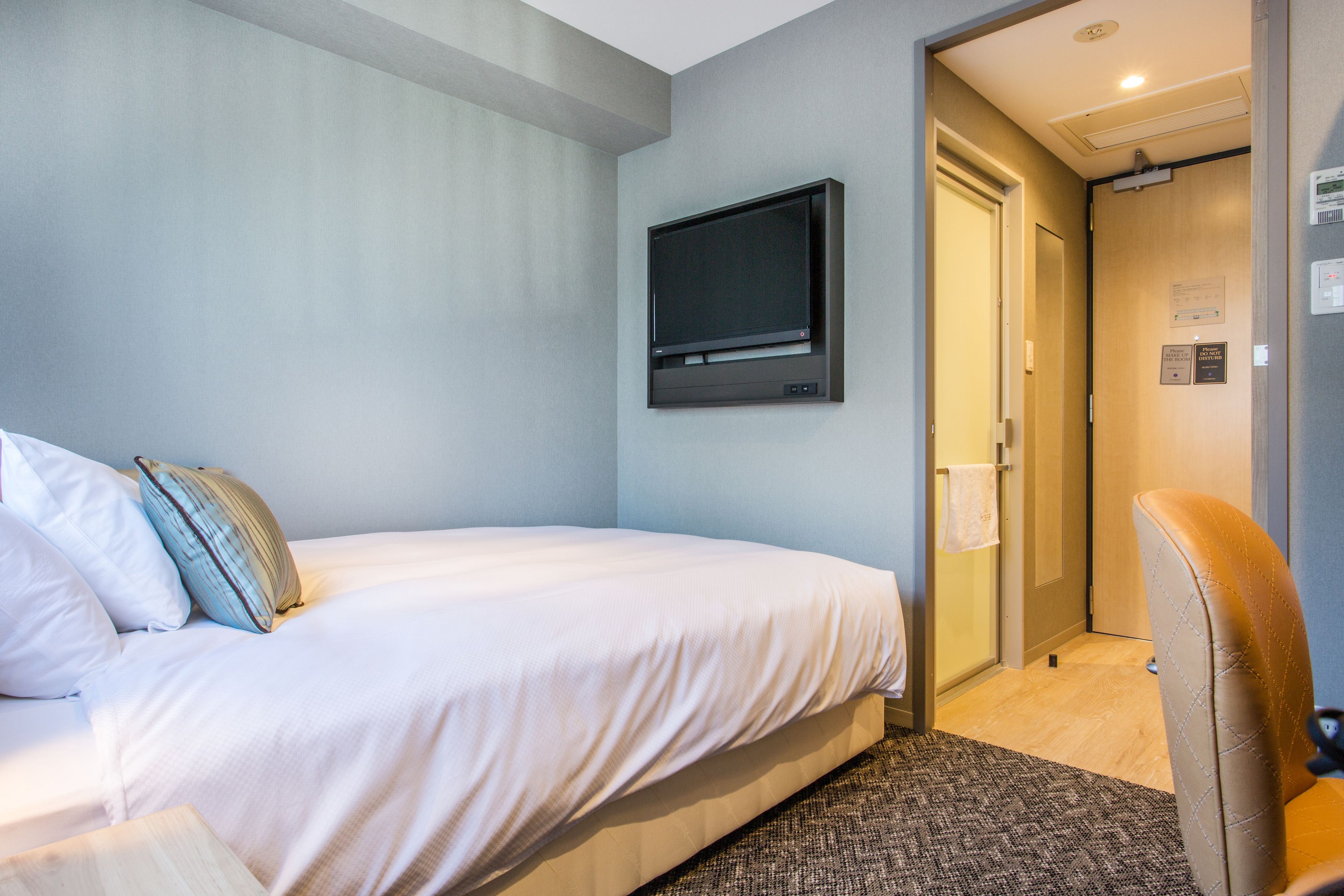 A hotel room with a bed, a mounted television, a door, and a chair.