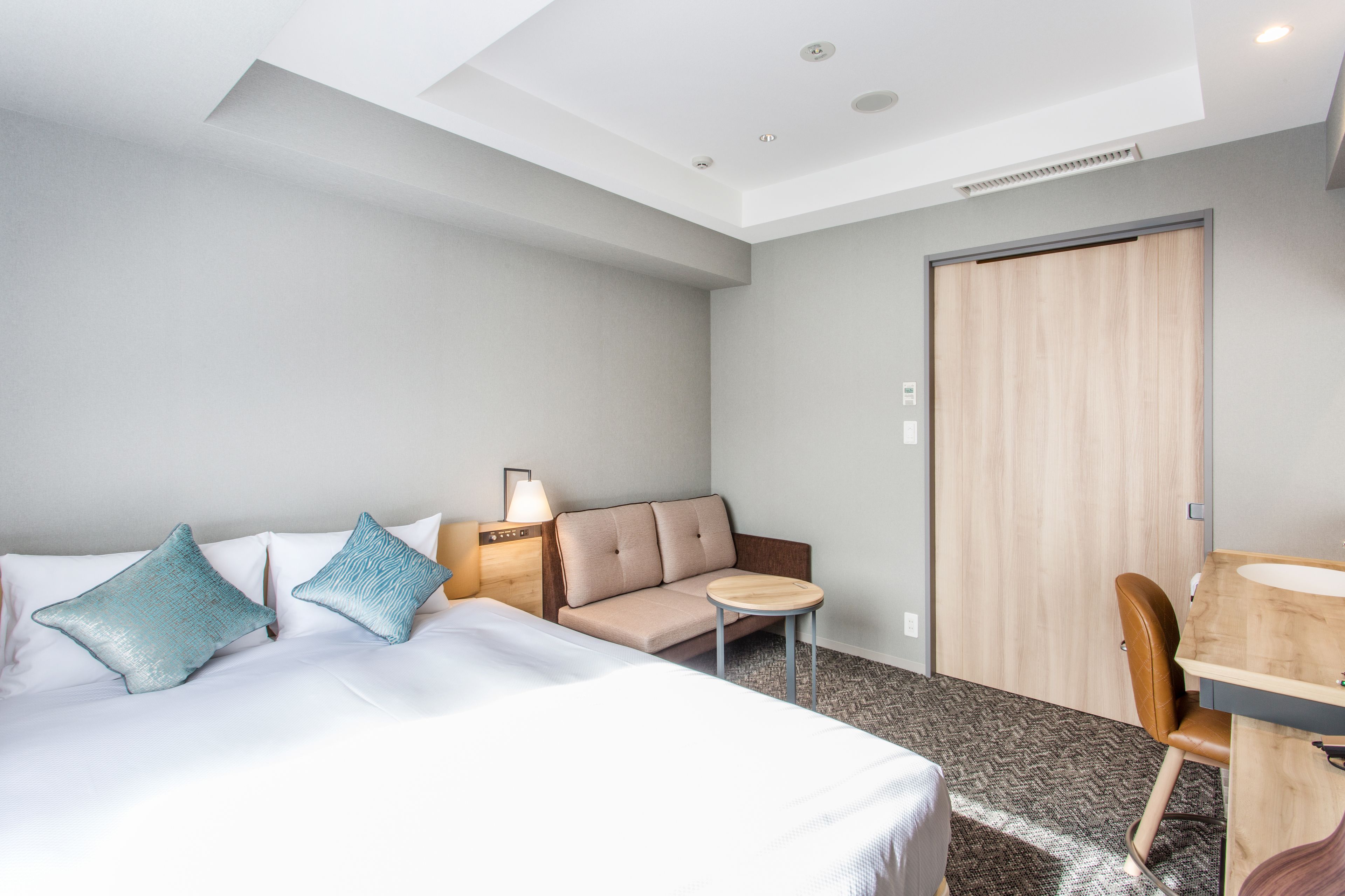 A hotel room with a bed, a sofa, a small table, a chair, and a desk with a sink.