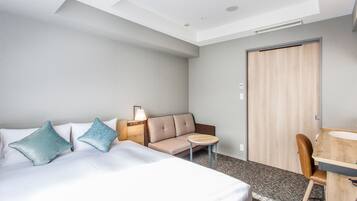 A hotel room with a bed, a sofa, a small table, a chair, and a desk with a sink.