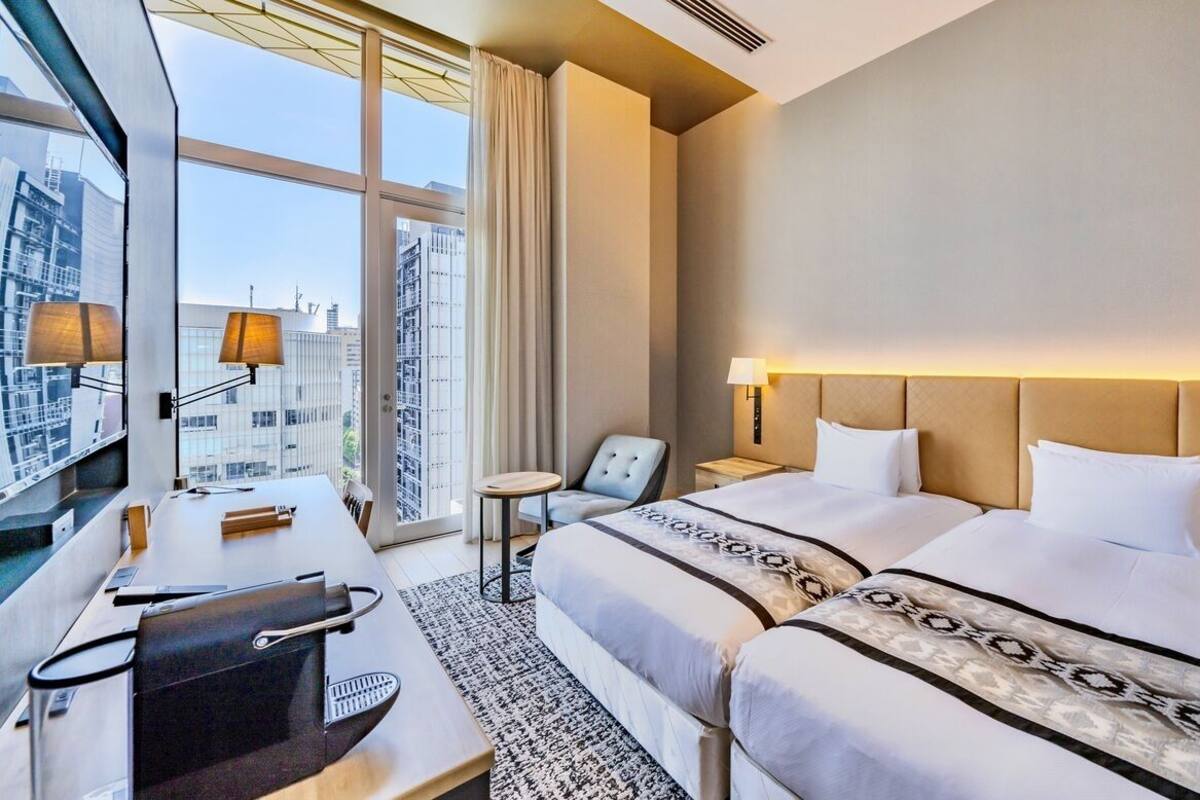Une chambre d’hôtel avec deux lits, un bureau, une chaise et une grande fenêtre donnant sur la ville.