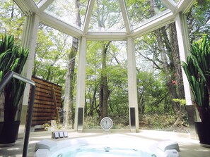 A glass-enclosed hot tub area with a clock, surrounded by trees and potted plants. - Cozy Inn Antique (Nasu)