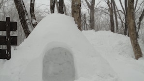Una estructura de iglú cubierta de nieve con un cartel de madera cercano.