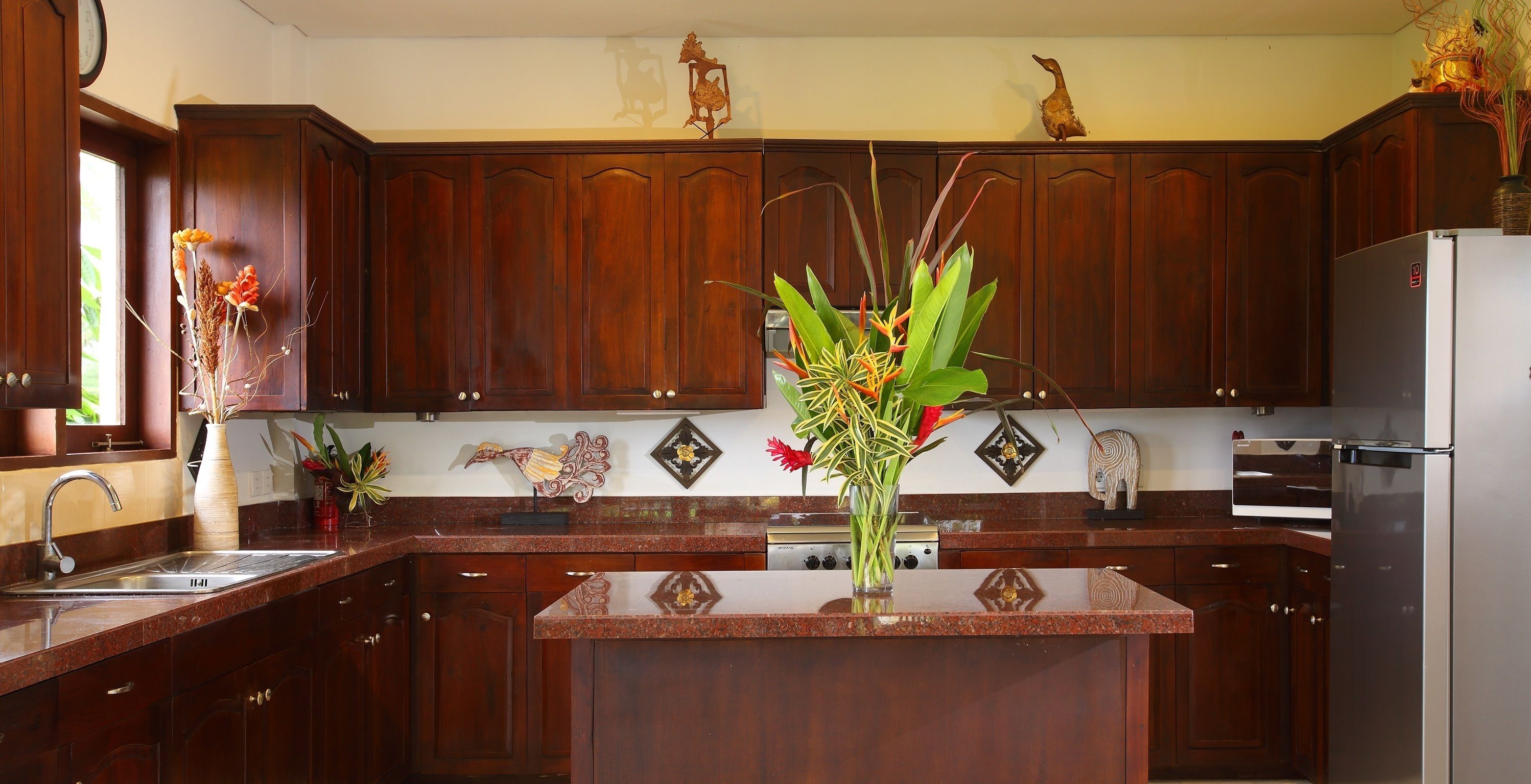 A kitchen with dark wooden cabinets, a granite countertop, and a central island with a vase of flowers.