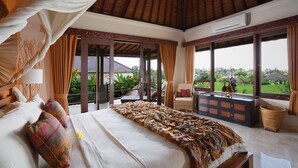 Un dormitorio amplio con una cama grande, una mesita de noche, una silla de mimbre y vistas al jardín a través de amplias ventanas.