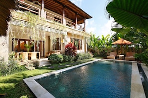 A poolside area with a pool, lounge chairs, and a covered seating area. - Satori Villas Bali (Ubud)