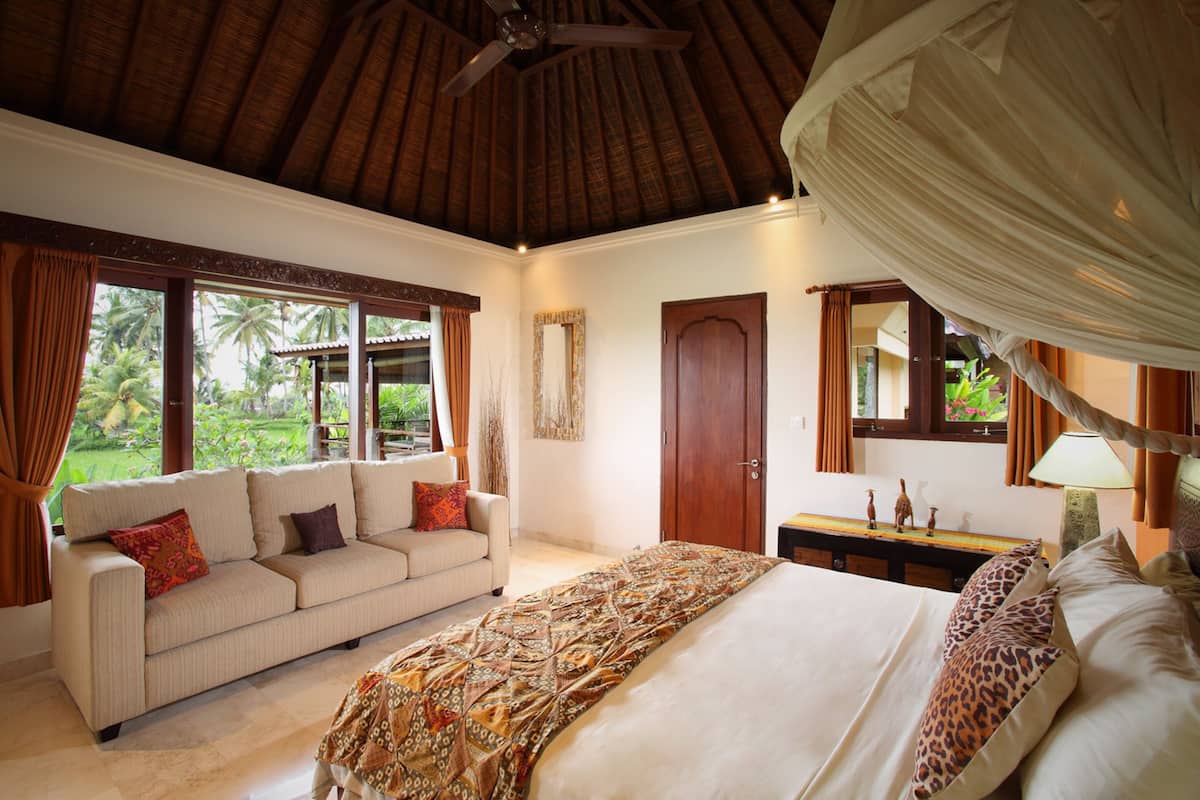 A bedroom with a bed, a sofa, a wooden door, and a window with curtains.