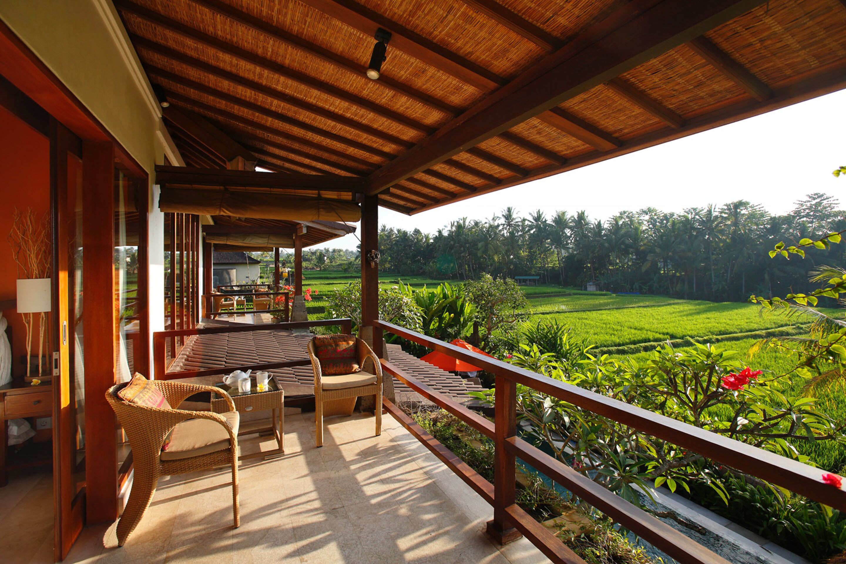 A covered outdoor area with a wooden ceiling, wicker furniture, and a view of a lush green landscape.