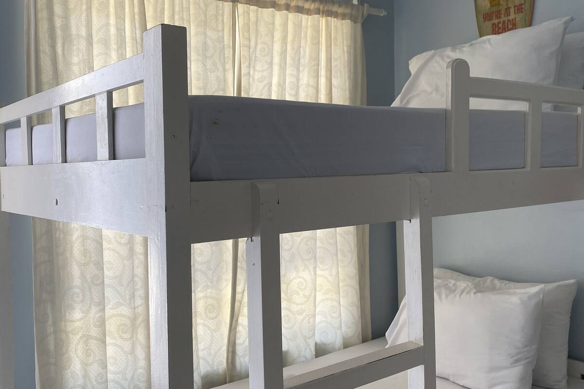 A bunk bed with a white headboard and footboard, a window with patterned curtains, and a wall with a 'Relax' sign.