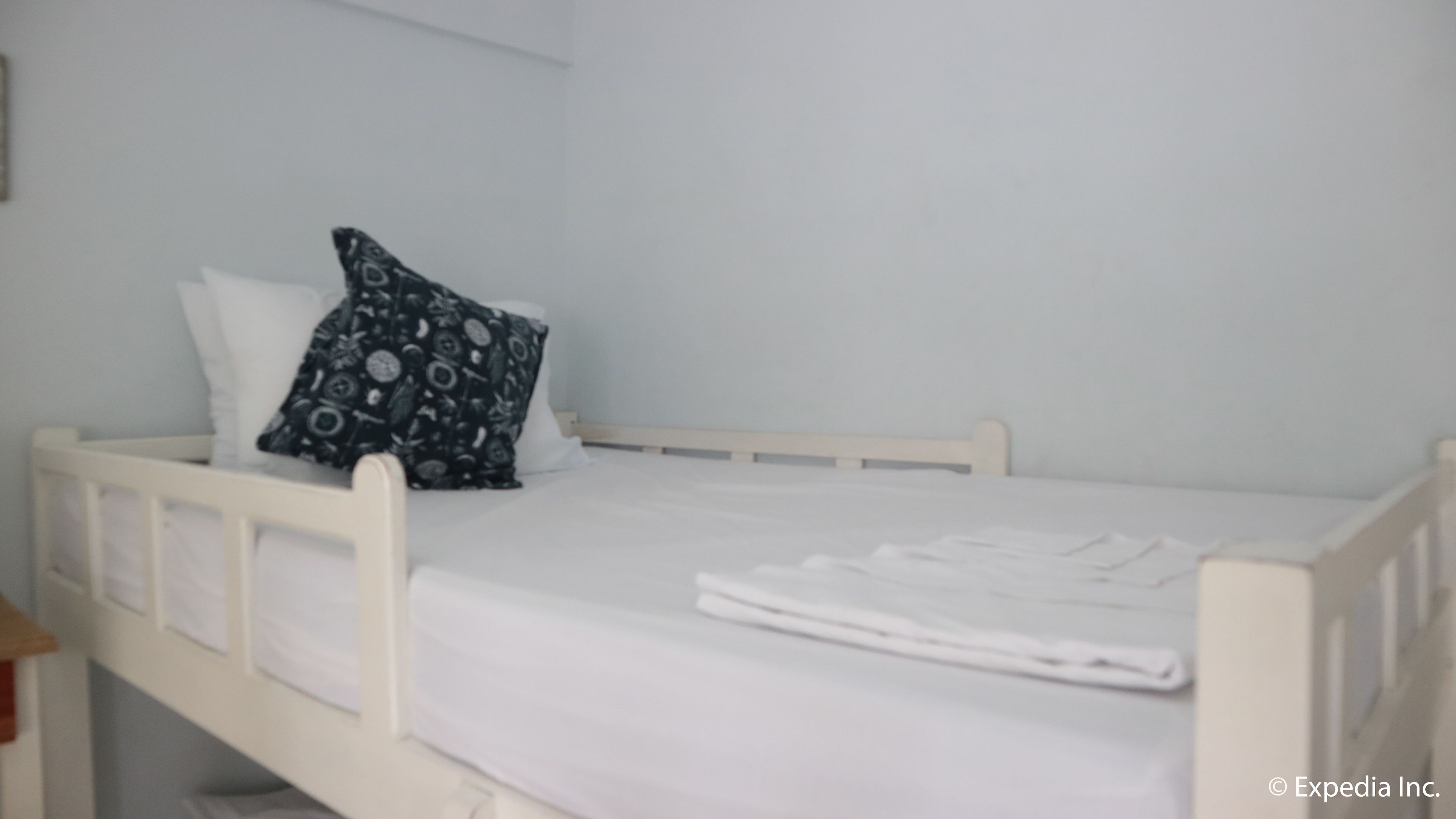 A white single bed with a black patterned pillow and a white blanket.