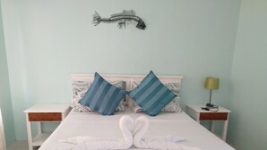 A neatly made bed with two pillows, a bedside lamp, and a decorative fish wall hanging. - Oceana Lodge (Baler)
