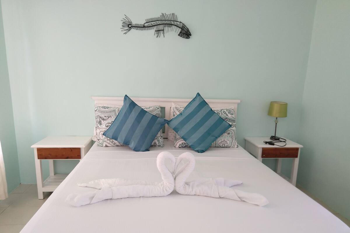 A neatly made bed with two pillows, a bedside lamp, and a decorative fish wall hanging.
