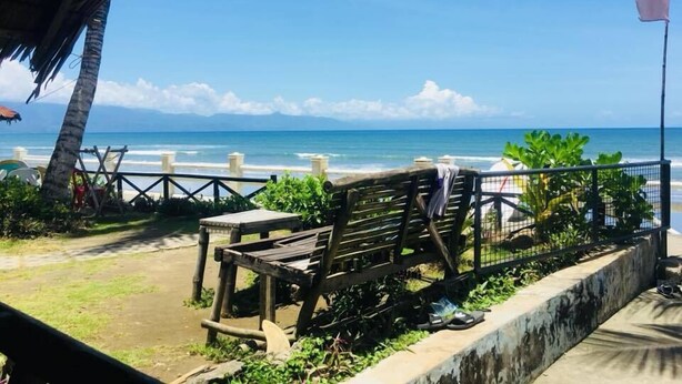 A beach view with a wooden bench, a thatched roof structure, and a flag. - Oceana Lodge (Baler)