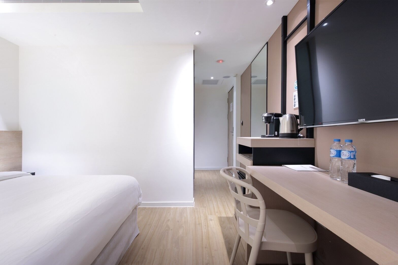 A modern hotel room with a bed, a desk with a chair, a flat-screen TV, and a coffee maker.