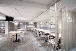 Un restaurante moderno con varias mesas y sillas, un televisor en la pared, y una pared de madera con un letrero.
