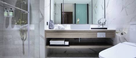 Un baño moderno con cabina de ducha de vidrio, tocador de madera, espejo grande y retrete.
