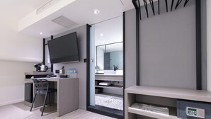 Een moderne hotelkamer met een bureau, stoel, televisie en een zichtbare badkamer door een glazen deur.