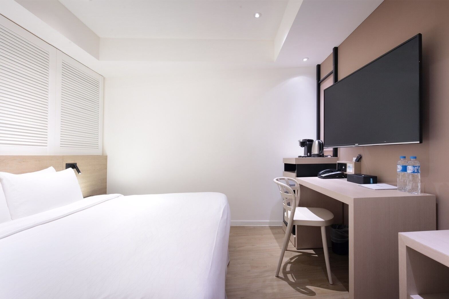 A hotel room with a bed, desk, chair, and a large flat-screen TV mounted on the wall.