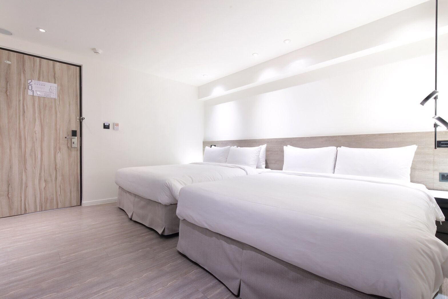 Une chambre d’hôtel moderne équipée d’un lit double, d’un lit simple, d’une porte en bois et d’un luminaire.