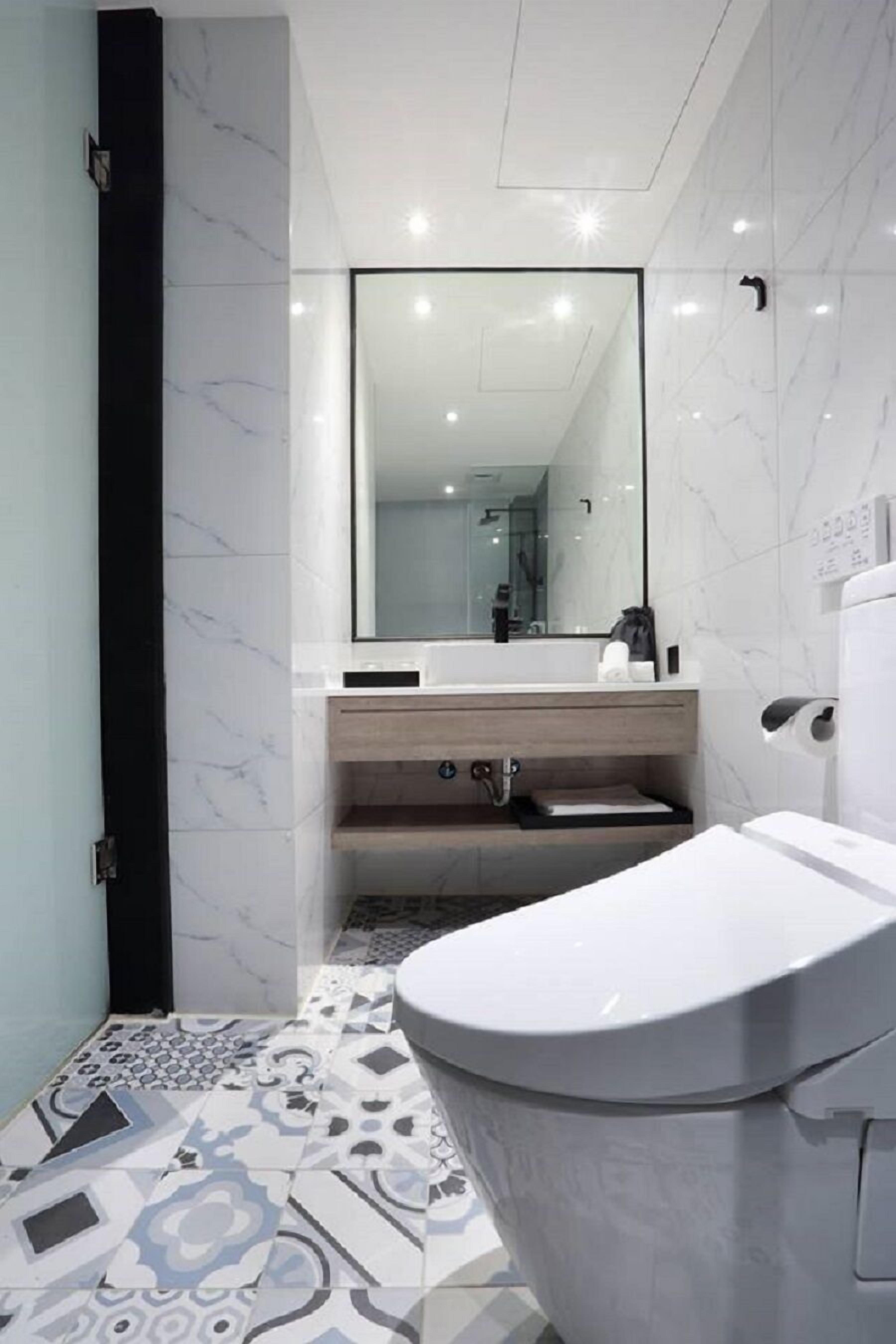 A modern bathroom with a white toilet, a mirror, and a sink with a wooden countertop.