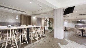 Een moderne eethoek met houten tafels en stoelen, een bakstenen muur en een flatscreen televisie aan de wand.