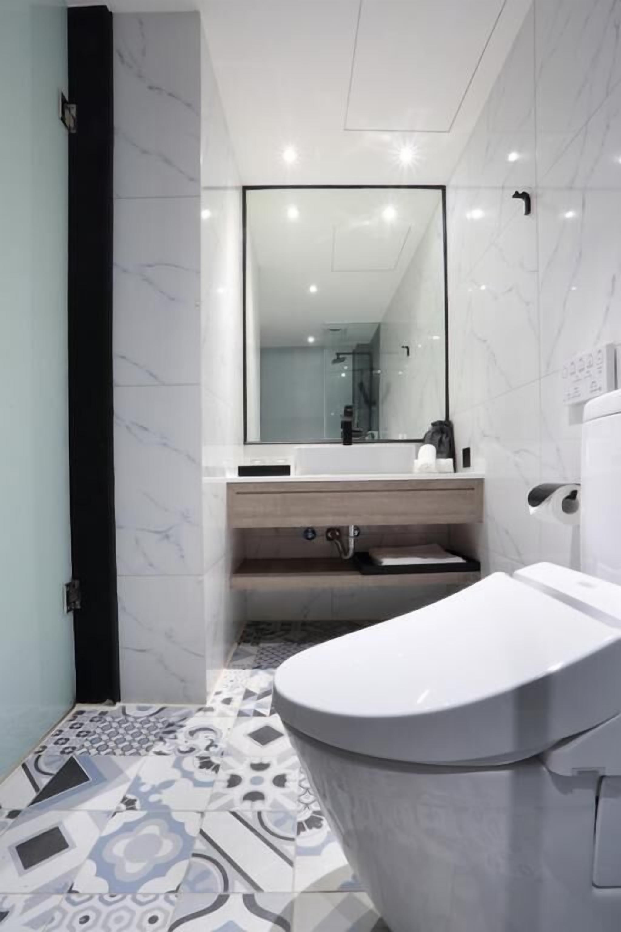 A modern bathroom with a white toilet, a mirror above the sink, and patterned floor tiles.