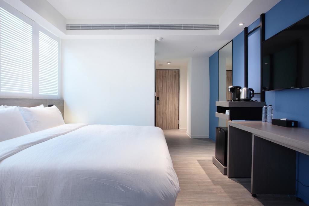 A modern hotel room with a large bed, a desk with a coffee maker, and a TV mounted on the wall.