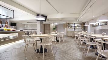 A modern restaurant with wooden flooring, white chairs, and tables.