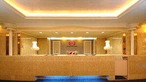 A reception area with a reception desk, two lamps, a floral arrangement, and a logo on the wall. - Grand Park Hotel Excel Kisarazu (Kisarazu)