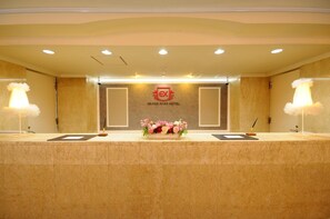 Eine Rezeption im Grand Park Hotel mit floralem Mittelstück, zwei Lampen und einem Logo an der Wand.