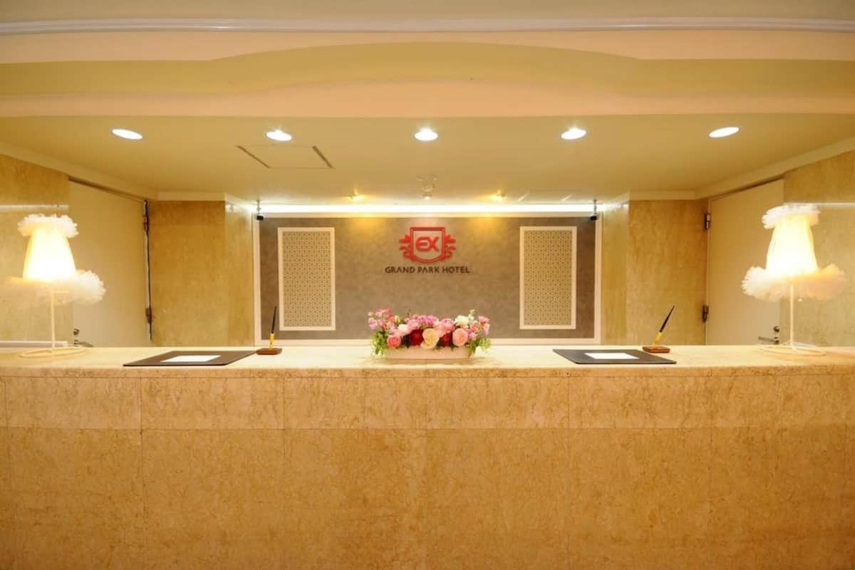 A reception desk at Grand Park Hotel with a floral centerpiece, two lamps, and a sign above.