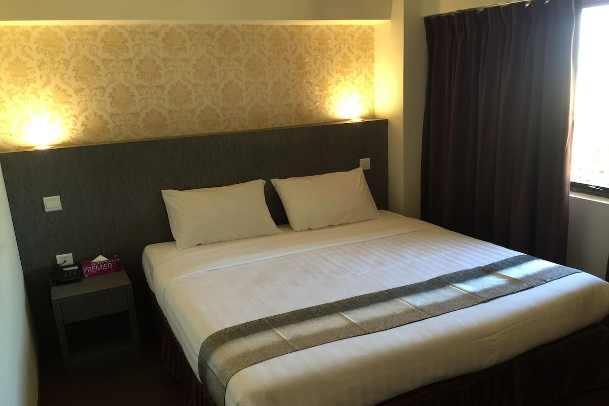 A neatly made bed with a headboard, a bedside table with a lamp, and a patterned wallpaper.