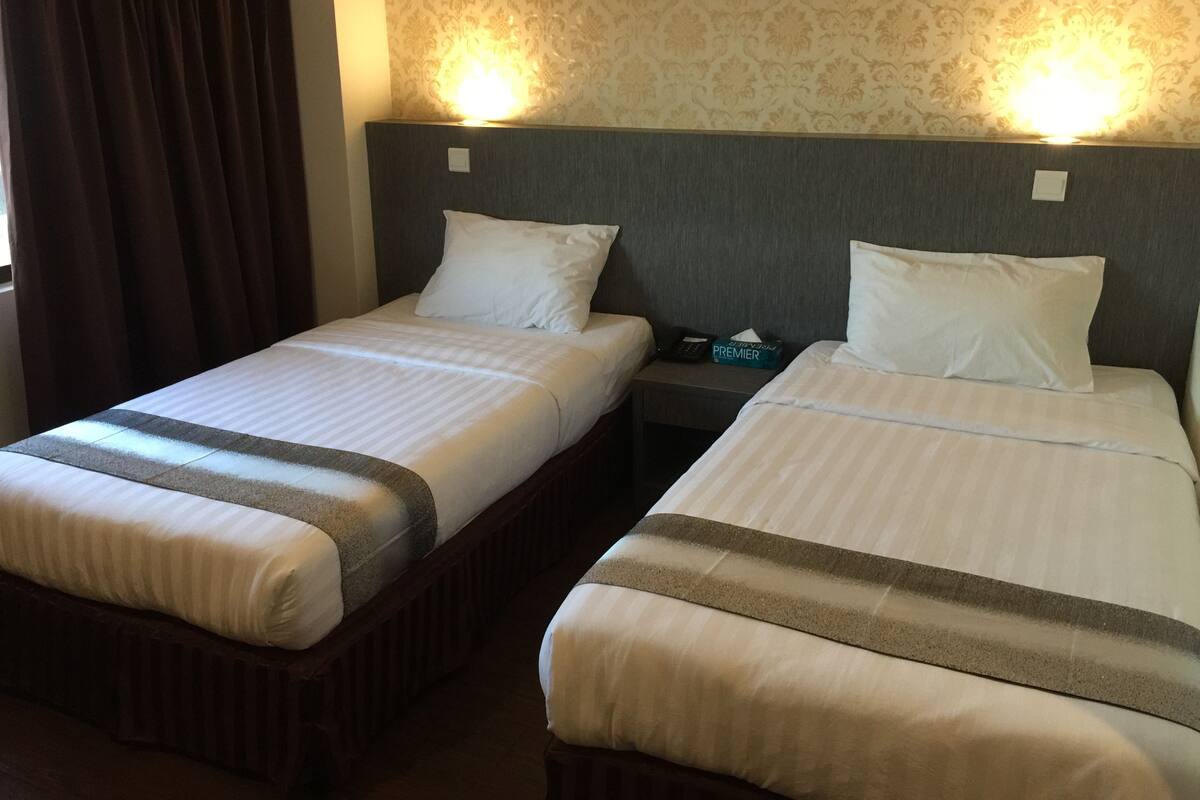 Two single beds with headboards, a nightstand with a phone and a box of tissues, and a patterned wallpaper on the wall.