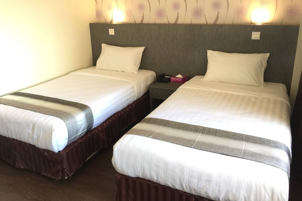 Two twin beds with white linens and striped blankets, a bedside table with a phone and a pink tissue box, and a wall with a floral wallpaper pattern.