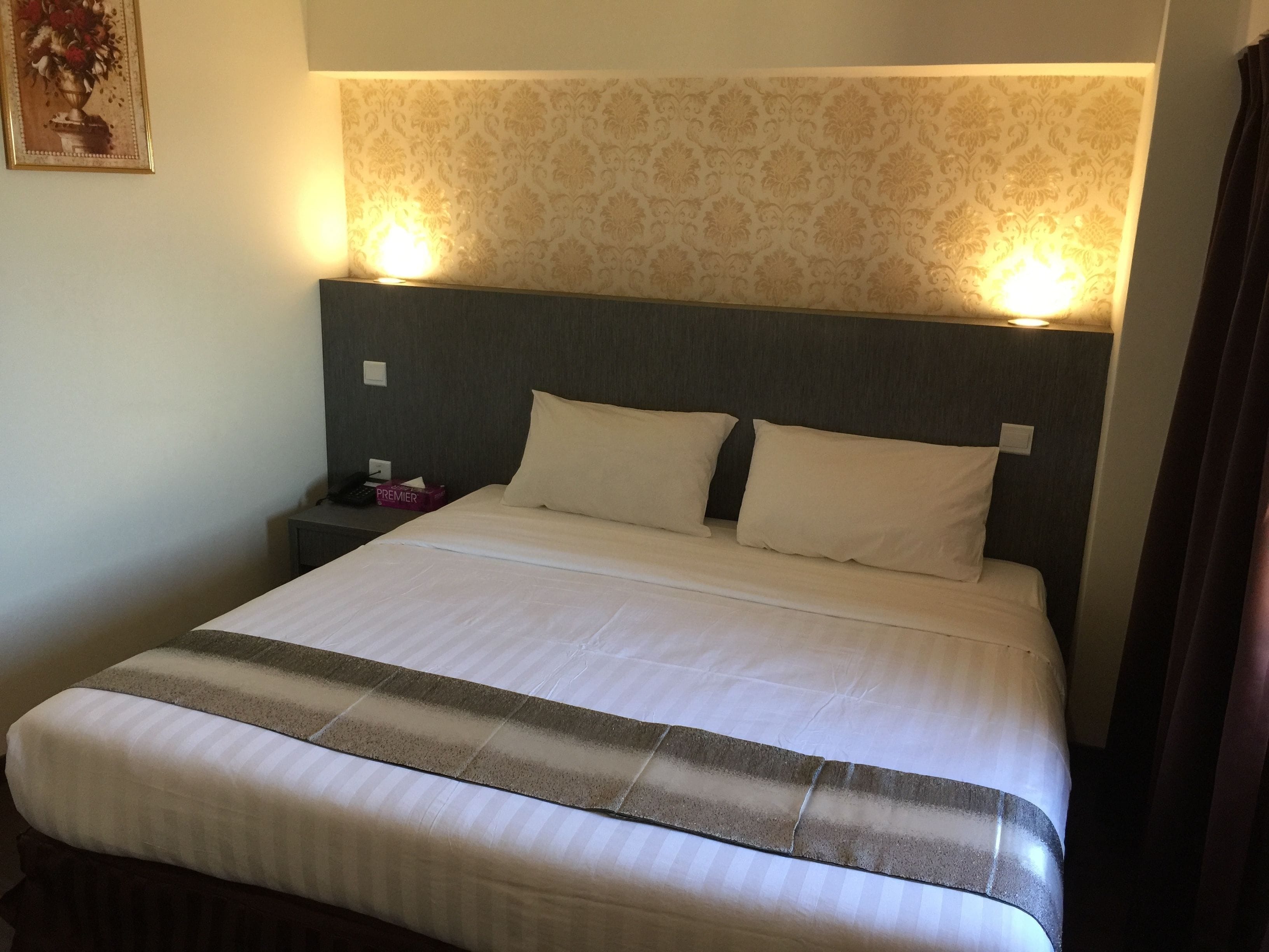 A hotel room with a large bed, two bedside tables, a nightstand, and a wall-mounted lamp.