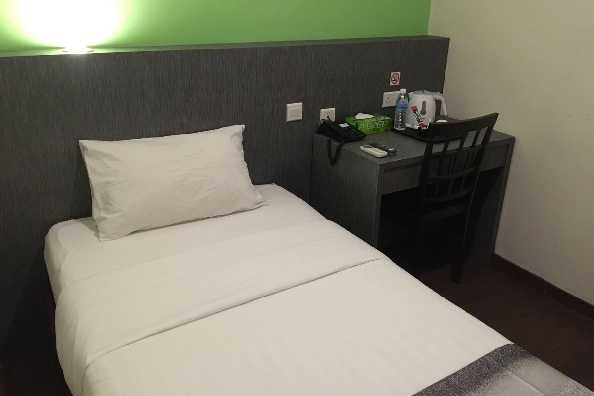 A hotel room with a bed, a desk, a chair, a telephone, a water bottle, and a box of tissues.