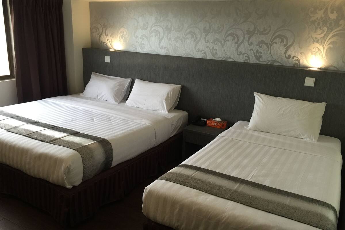 Two double beds with white linens and striped bedspreads, a nightstand with a phone and a box of tissues, and a patterned headboard.