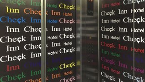 En hotellhiss vars väggar är täckta av upprepade texter som lyder: ”Check Inn Hotel Check”.