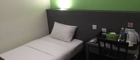 A single bed with white bedding, a bedside table with a phone, a water bottle, a box of tissues, and a kettle.