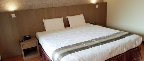 Una cama bien hecha con edredón blanco y almohada decorativa, una mesita de noche de madera con un teléfono, y un papel tapiz con estampado sobre la cama.