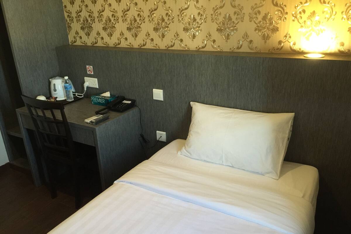 A hotel room with a bed, a desk, a chair, a telephone, and a wall with a floral pattern.